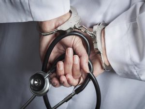 hands in cuffs, holding a stethoscope, wearing a white coat
