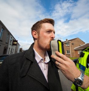 caucasian man blowing into breathalyzer being held for him