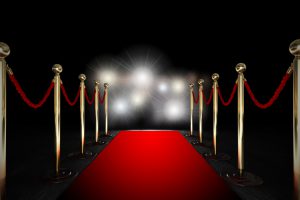 a red carpet leading between rope barriers toward camera flashes in the distance