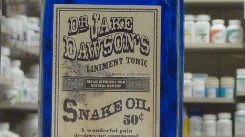 patent medicine label for "snake oil" in foreground with shelves full of supplements behind