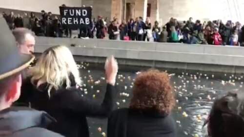 Protesters in front of pill-bottle litter, with "fund rehab" sign