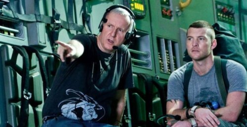 director James Cameron gestures to the distance with actor Sam Worthington sitting beside him looking in that direction, on the Avatar set
