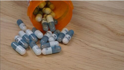 blue and white adderall capsules spilling out of an orange prescription bottle on a tabletop