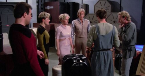 An Enterprise crew member looking at four people just beamed aboard and their cargo. Two are well-groomed, two scruffy-looking.