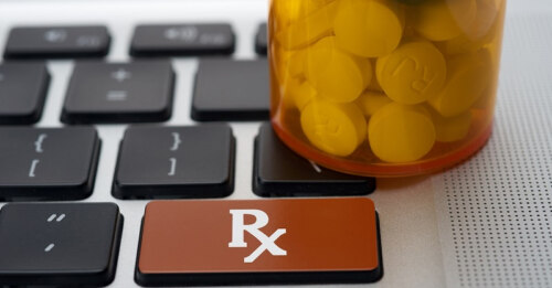 Keyboard with black keys, one red key labeled "Rx", and an amber bottle with pills in it sitting on keys