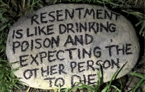 quote written on a rock in the grass: "resentment is like drinking poison and expecting the other person to die"