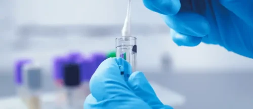 nitrile-gloved hands holding a swab over a sample tube
