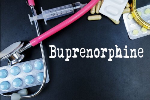 pills, stethoscope and syringe on dark table with text "Buprenorphine" in grainy white typeface