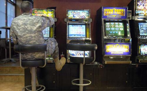 soldier in camo, back to the camera, sitting at a bank of slot machines