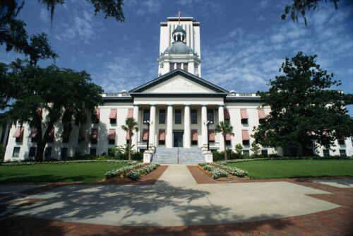 Florida state capitol building against a blue sky with trees and a plaza framing the shot