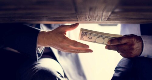 two men's hands, under a table - one hand open to receive the money the other hand is offering