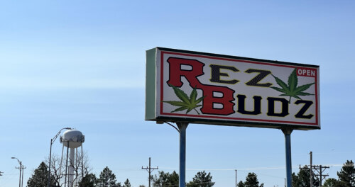 sign advertising "Rez Budz - Open" against blue sky with watertower and trees in background