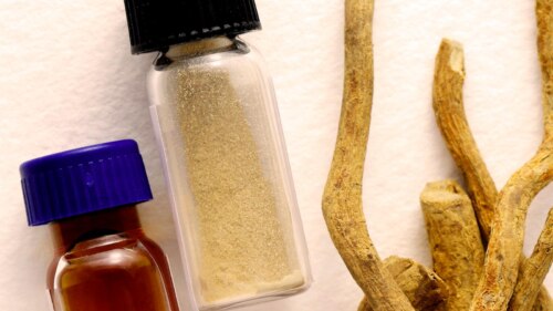 Two vials (one brown, one clear) filled with powder, next to several light brownish iboga roots