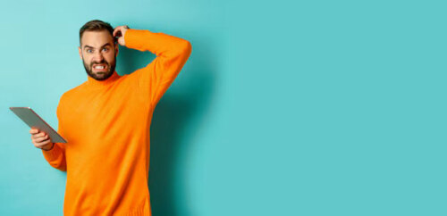 Dark-haired, bearded man holding tablet, wearing orange long-sleeve shirt, off-center to left against turquoise background, scratching his head and looking baffled.