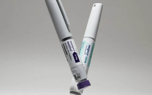 A Mounjaro dose injector and a Wegovy dose injector suspended at opposing angles against a gray background.